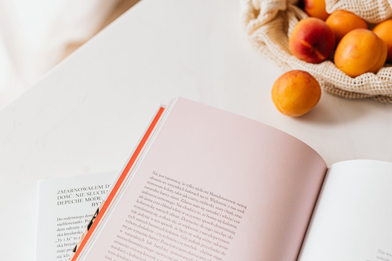 From above of opened book placed on white table near cotton sack with natural ripe apricots